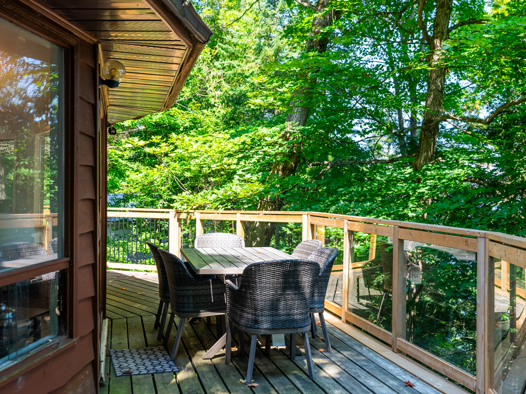 A wraparound deck with a table and chairs extends around the curving side of a round cottage.