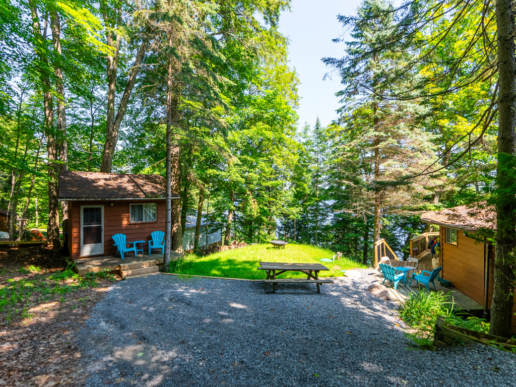 A wide gravel driveway with a picnic table leads to a round cottage and a small shed.