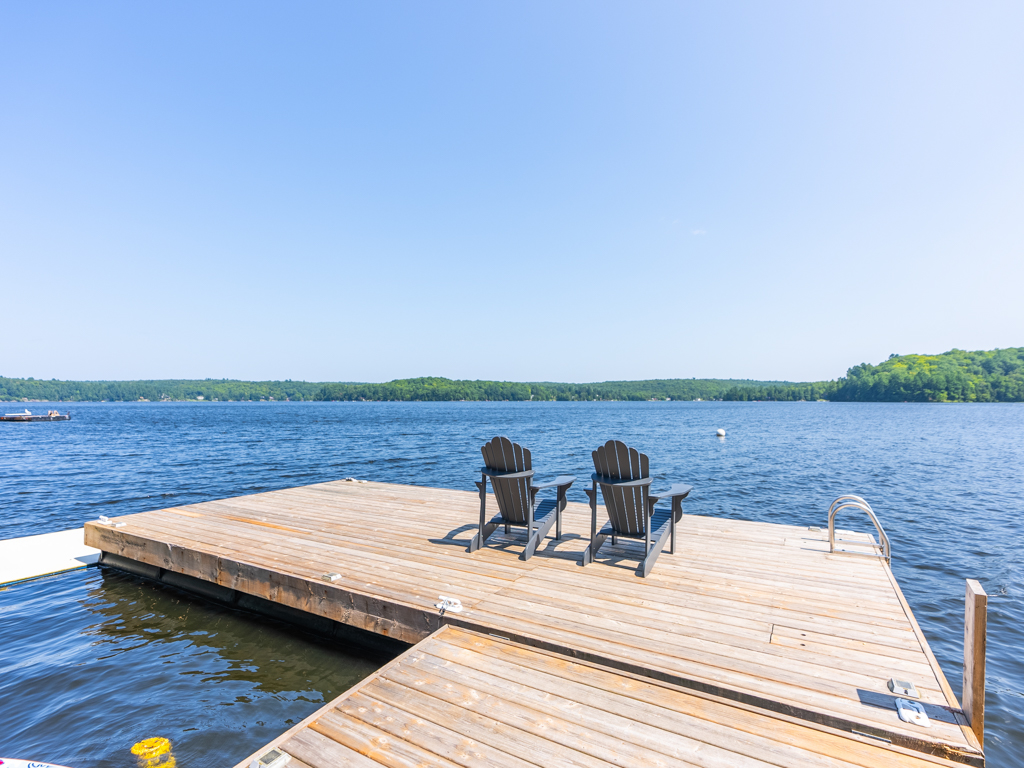 Two chairs sit on the end of a large dock, looking out across a lake.