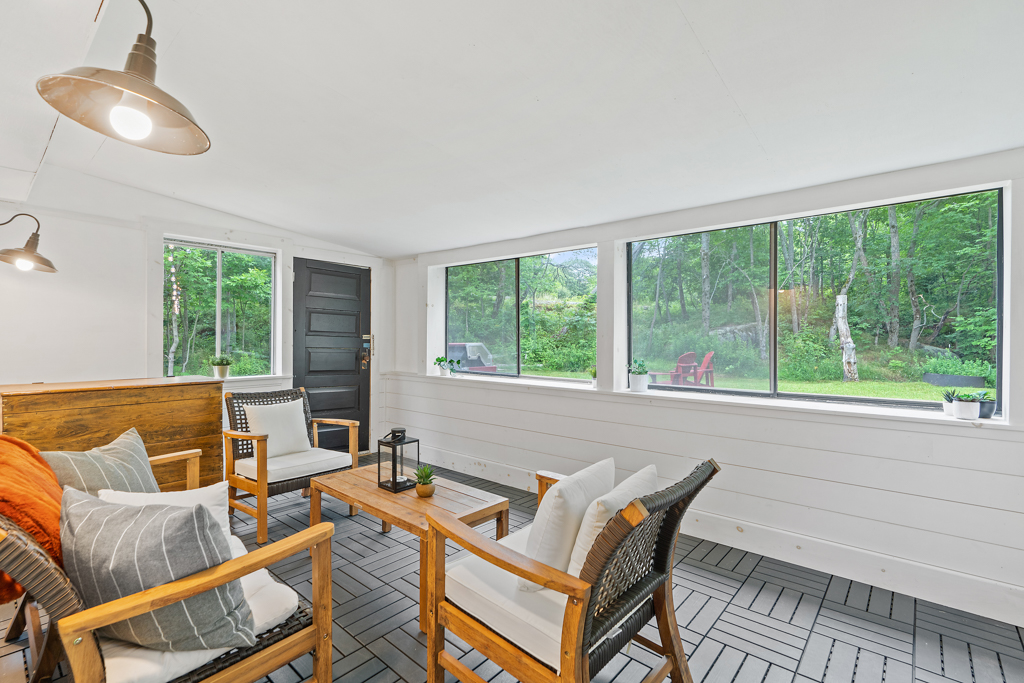 A bright sunroom sitting area with chairs, a couch, and lots of windows. A door leads to outside.