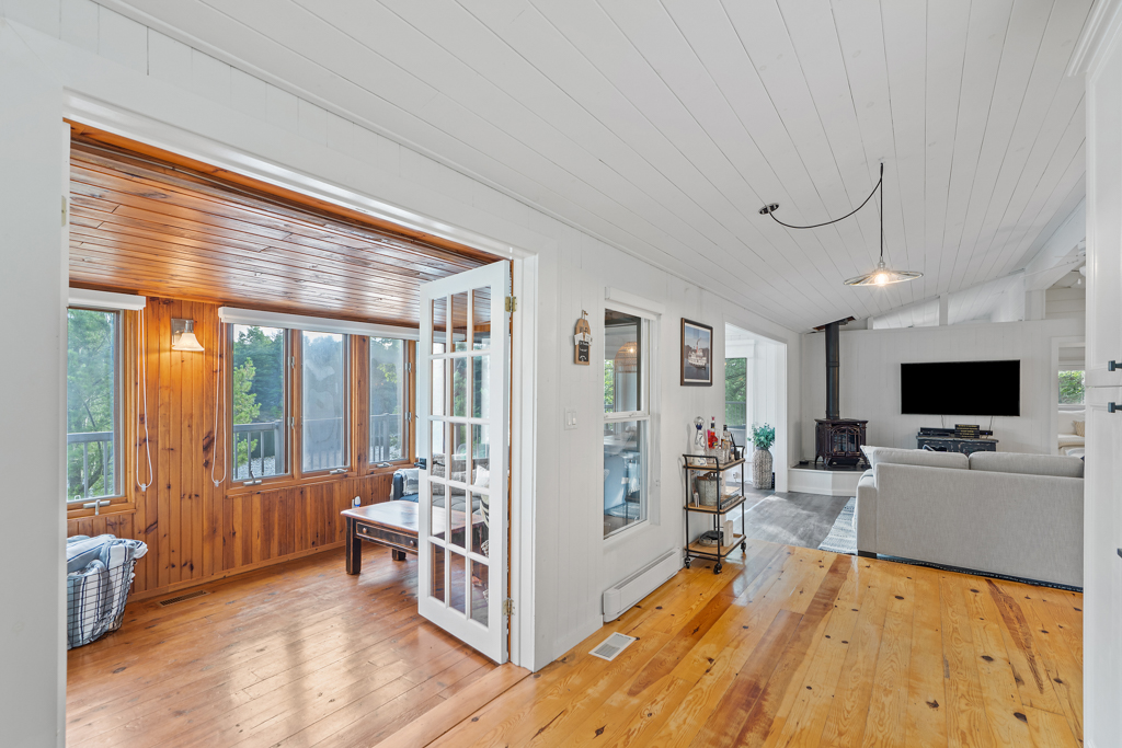 An open-concept cottage space with flow from the sunroom into a kitchen and living space. Hardwood flooring throughout.