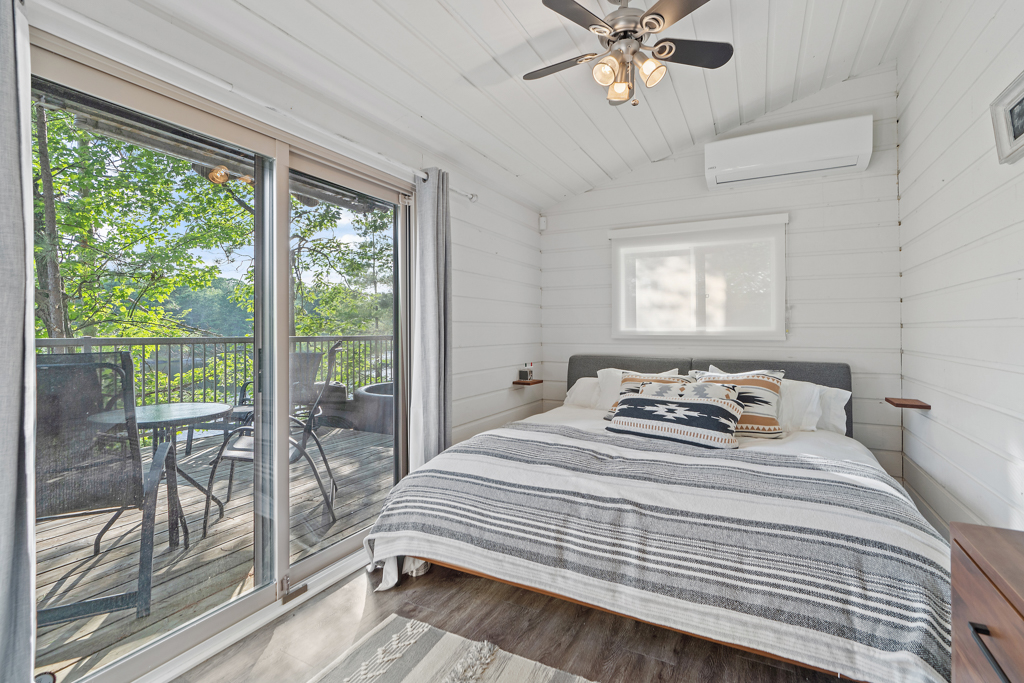 A bright bedroom with a big bed and double glass doors that lead out to a deck.
