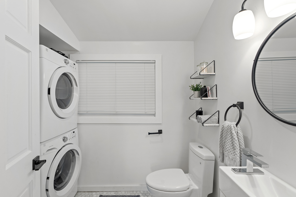 A bathroom and laundry space with a toilet and a stacked washing machine and dryer.