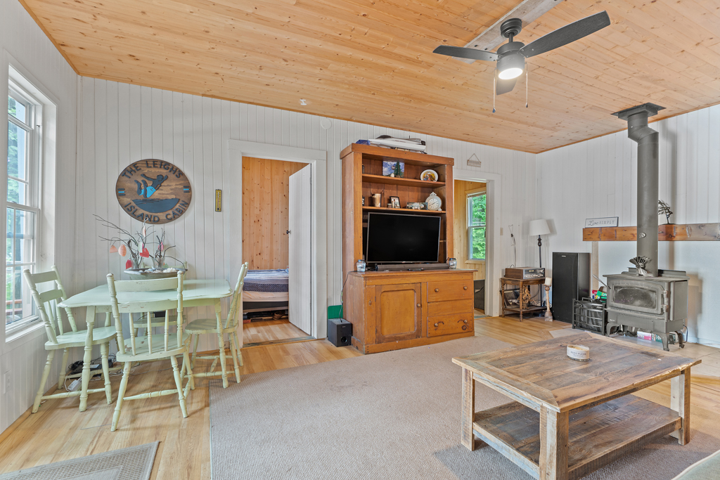 A bright, open cottage living space with a small dining table, a television, a couch, a coffee table, and a wood-burning fireplace.