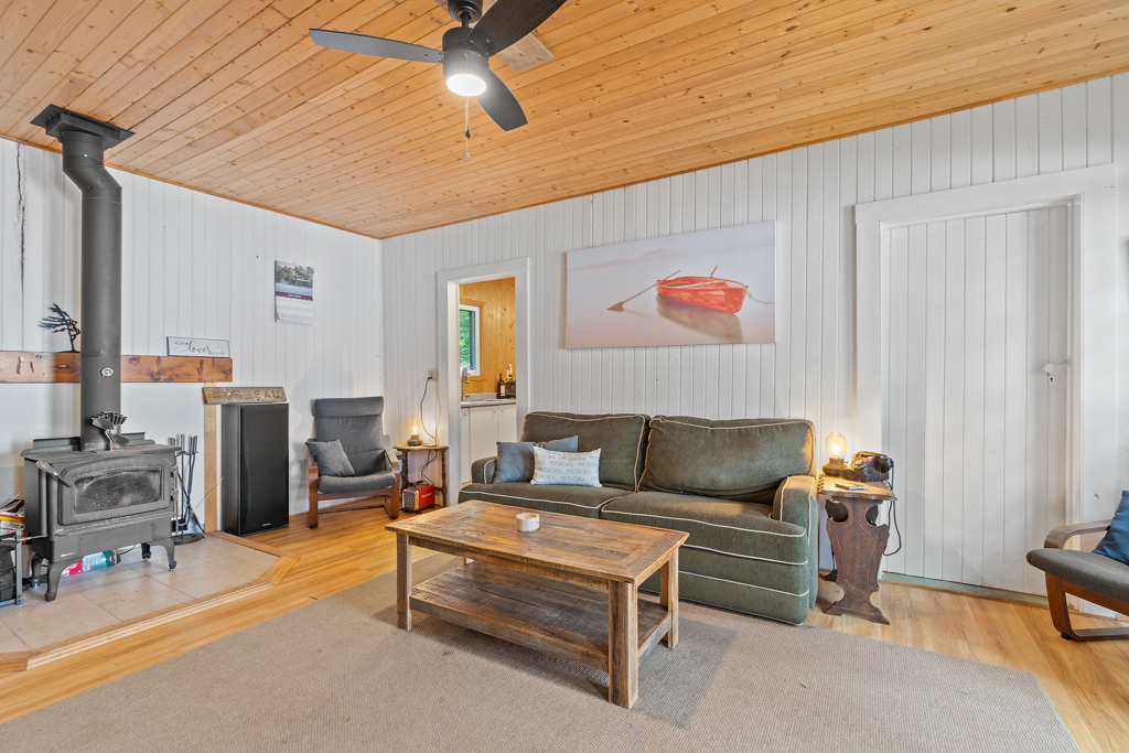 A bright, open cottage living space with a couch, a coffee table, and a wood-burning fireplace.