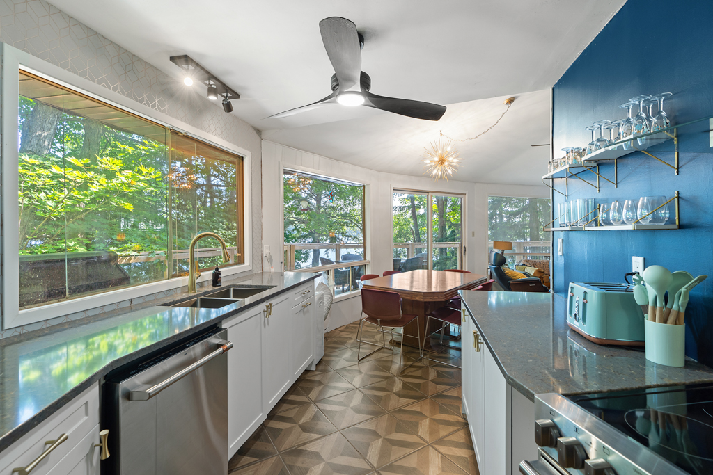 A kitchen with updated appliances leads into a bright dining area with a table and chairs. Lots of windows line the outer wall.