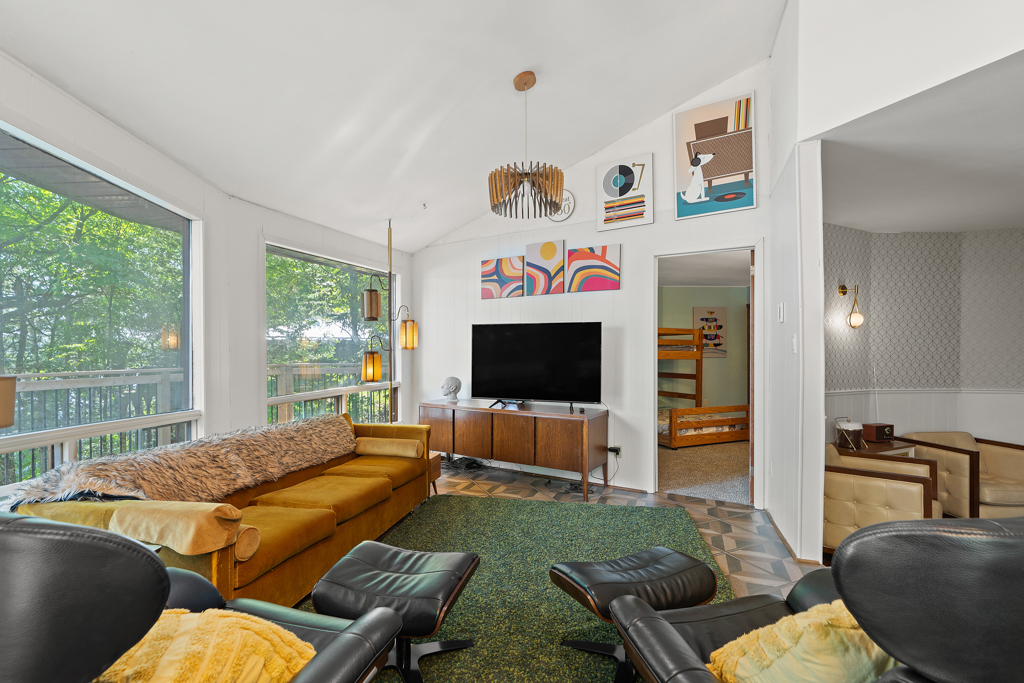 A living area with a couch, two chairs, large windows, and a television.