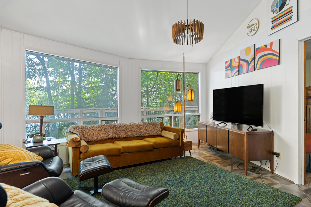 A living area with a couch, two chairs, large windows, and a television.