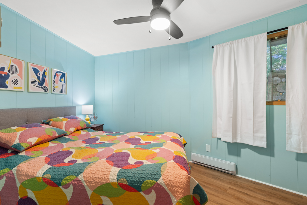 A bedroom with light blue walls and a bed with a brightly patterned bedspread.