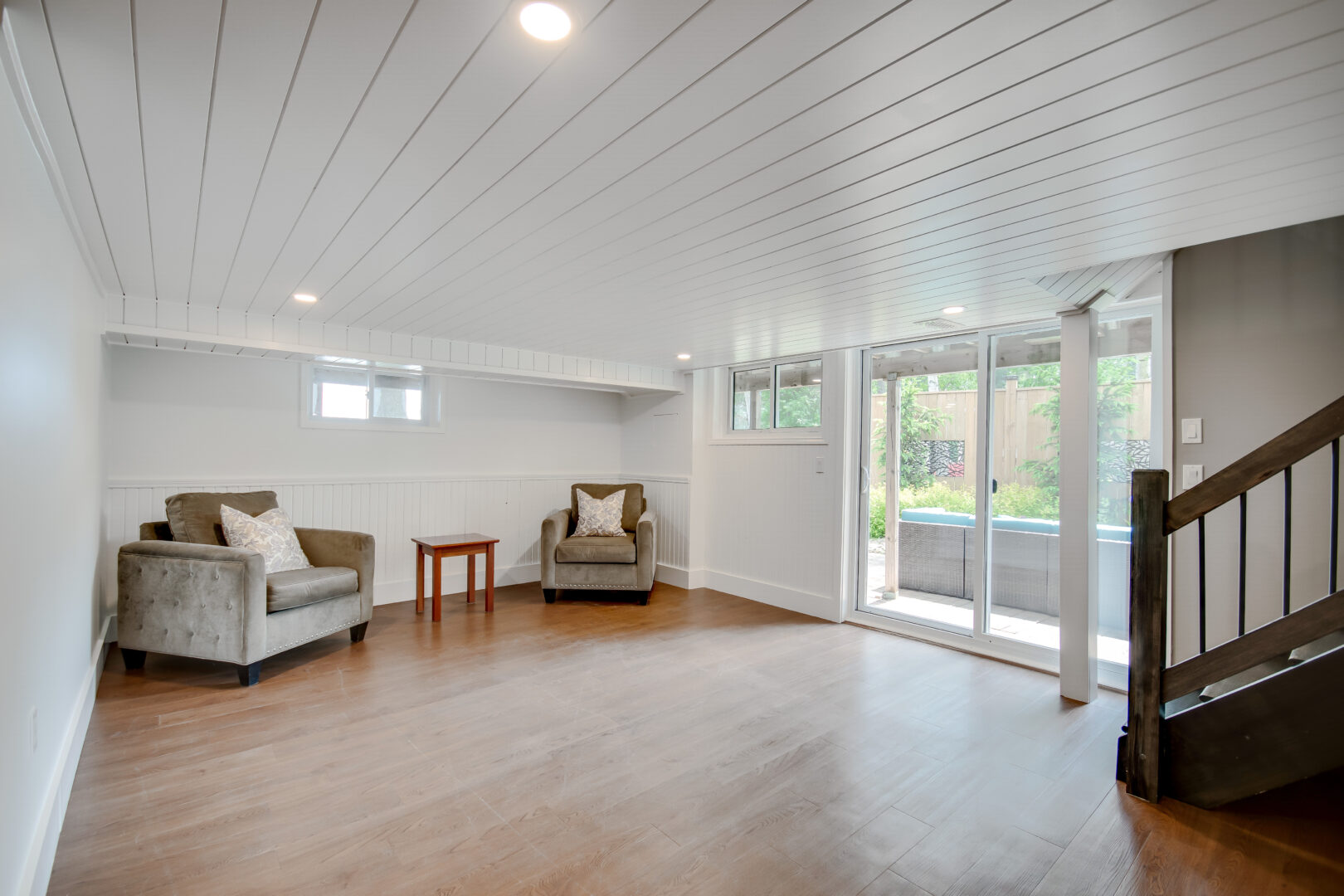 A bright, sparse lower level with two chairs, hardwood flooring, and double glass doors that walk out to a patio.