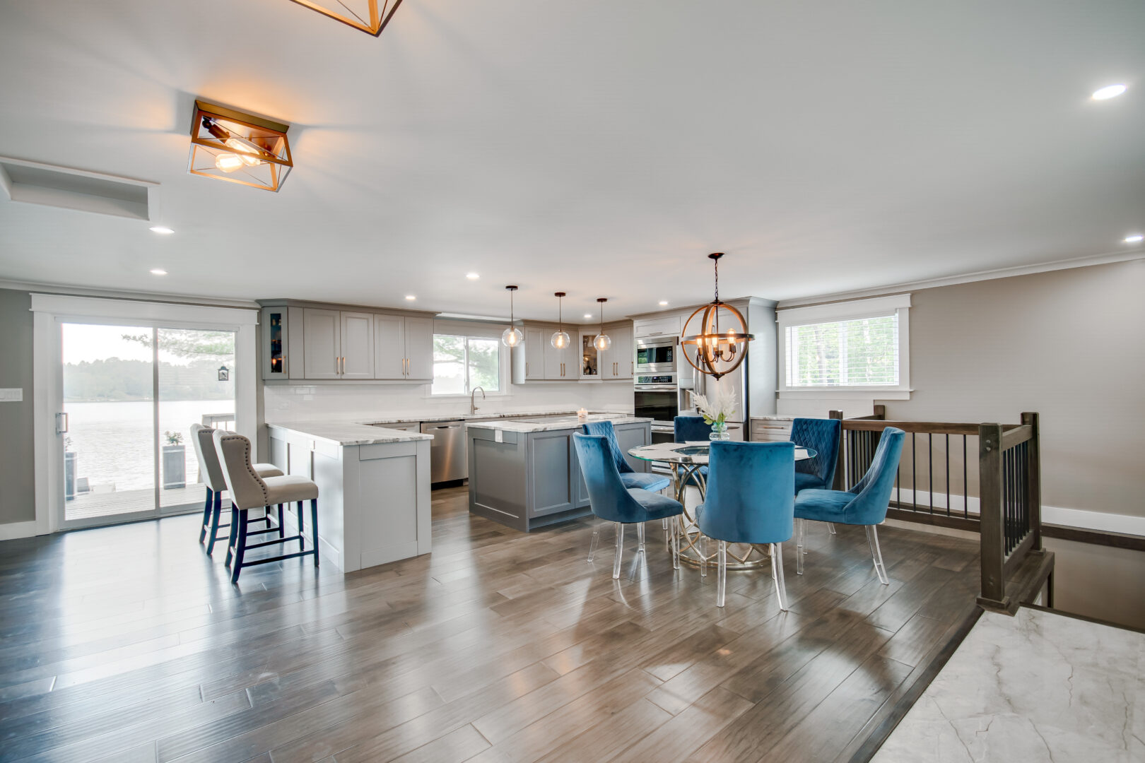 A bright, modern kitchen and dining area with hardwood floors, blue dining chairs, and metal light fixtures.