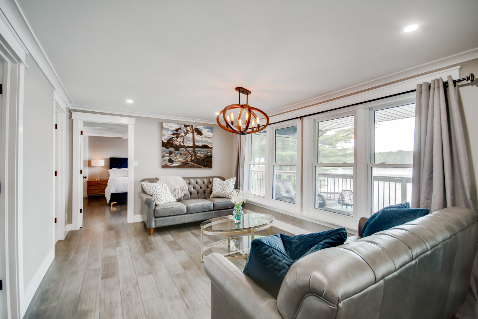 A bright living area with large windows, a modern metal light fixture, and two grey couches.