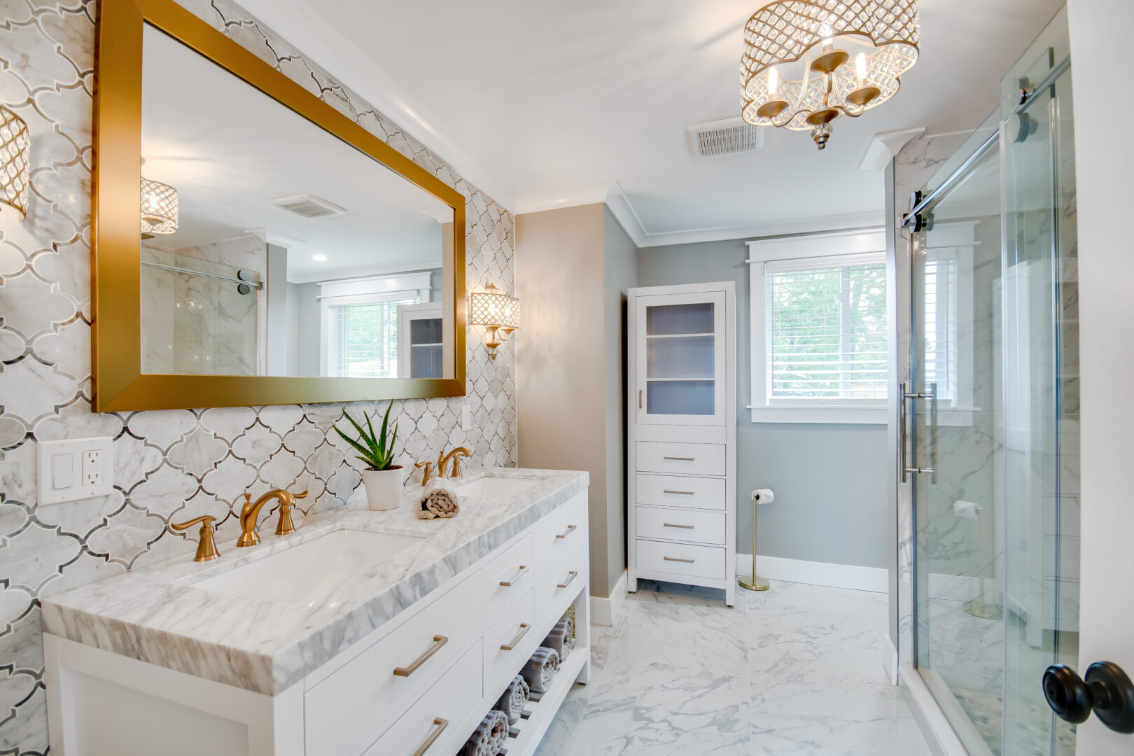 A large, bright bathroom with cupboards, a sink, a large mirror, and a big shower. Gold accents throughout.