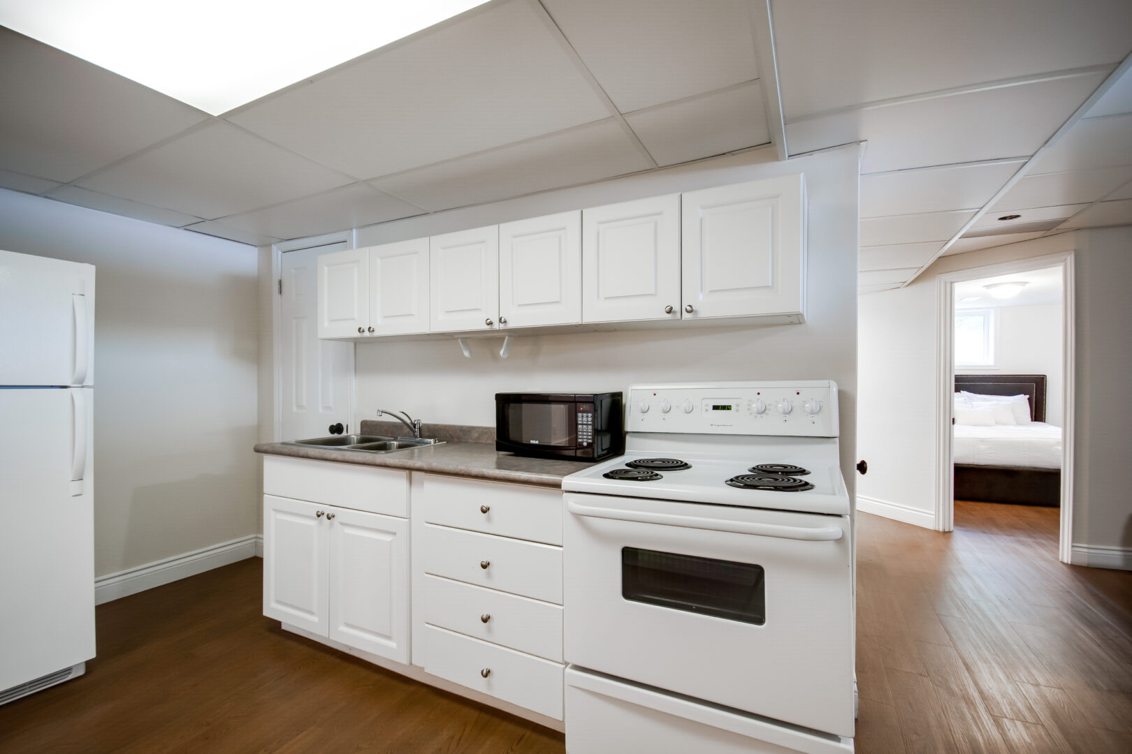 A small kitchenette area with white cupboards, a sink, and an oven.