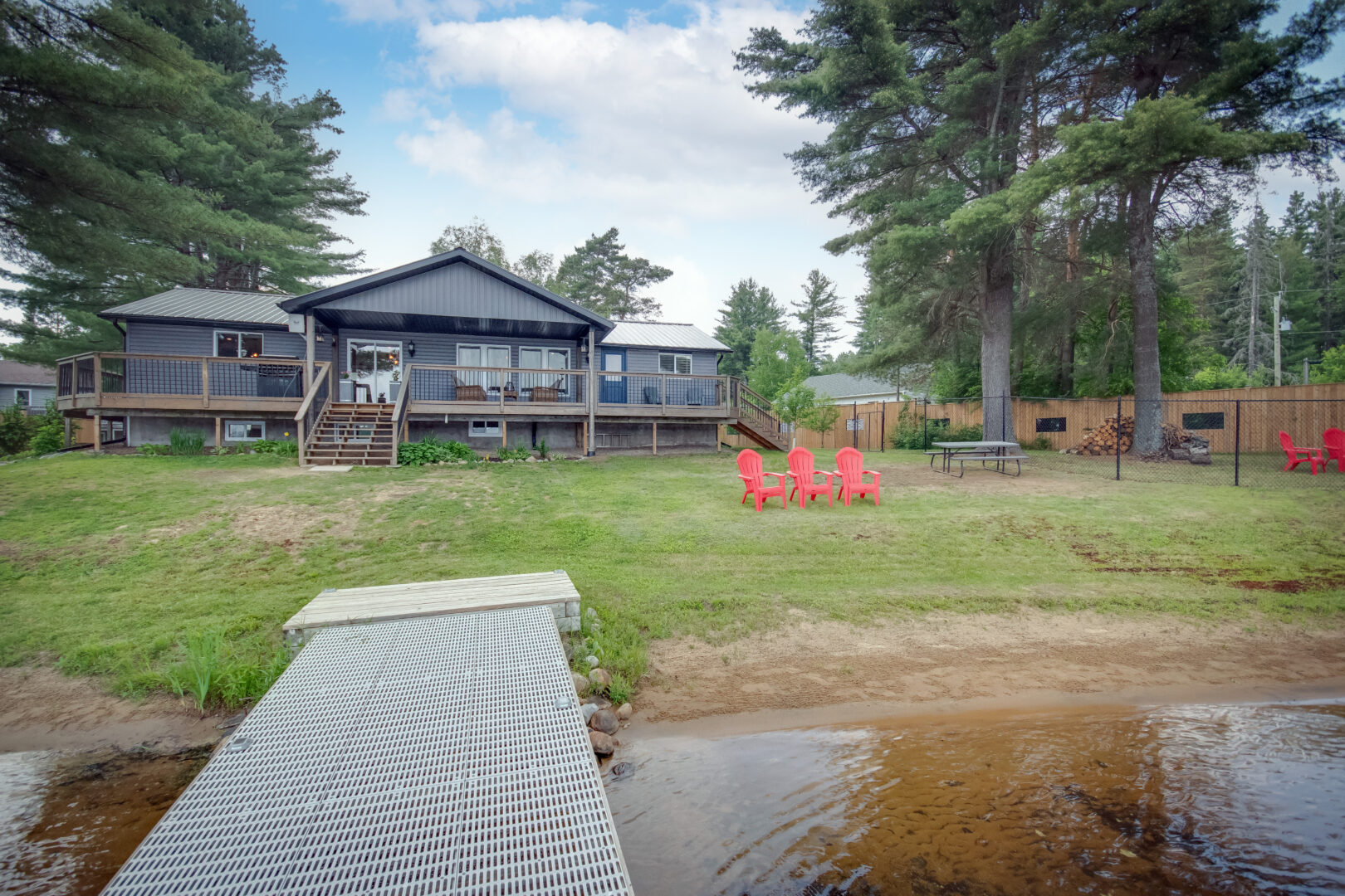 View up to a cottage bungalow from a metal dock on a sandy lake shore.