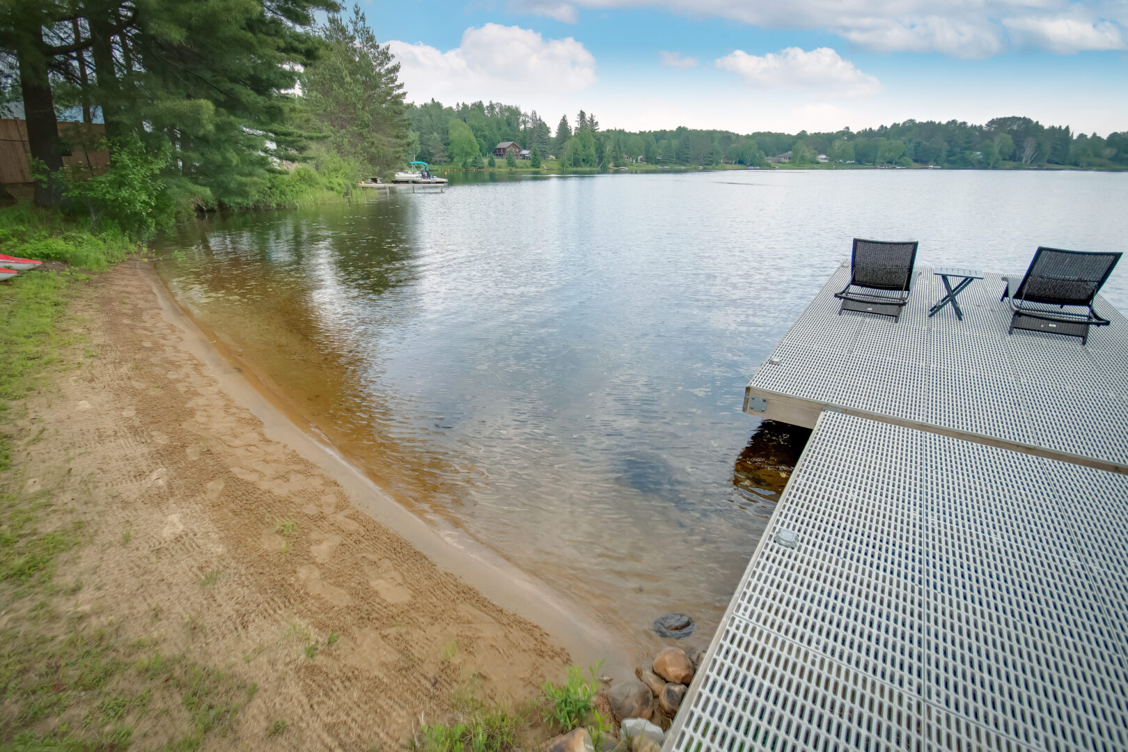 A metal dock branches off from a sandy, gently sloping shoreline of a lake.