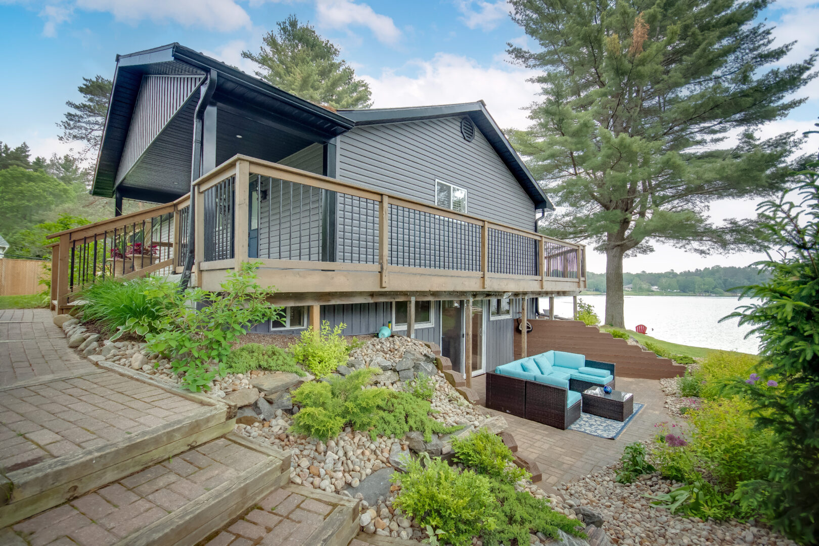The side of a cottage bungalow, with a patio branching out from a lower level walk-out.