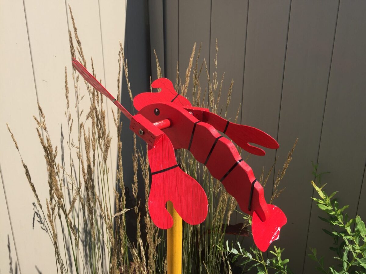 A lobster whirligig in a backyard garden