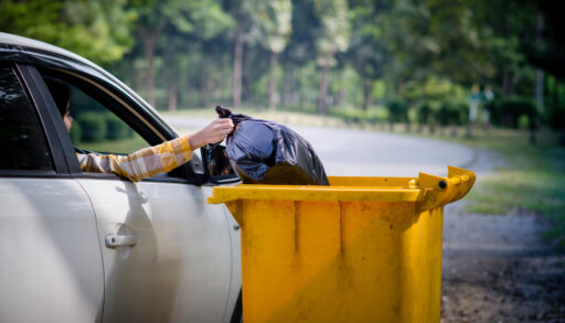 Driver throwing out a garbage bag from their car into a receptacle. Environmental conservation