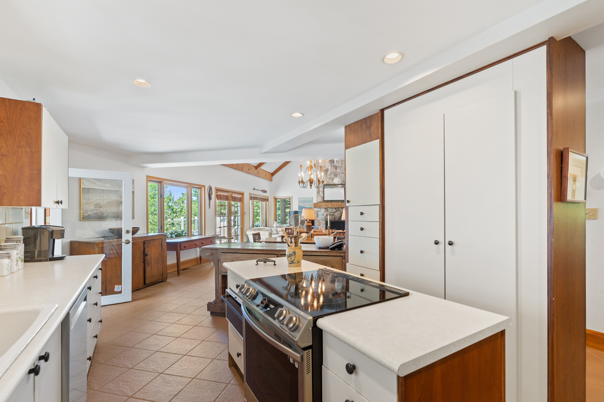 A bright kitchen with an island and white cupboards leads into a large living area.
