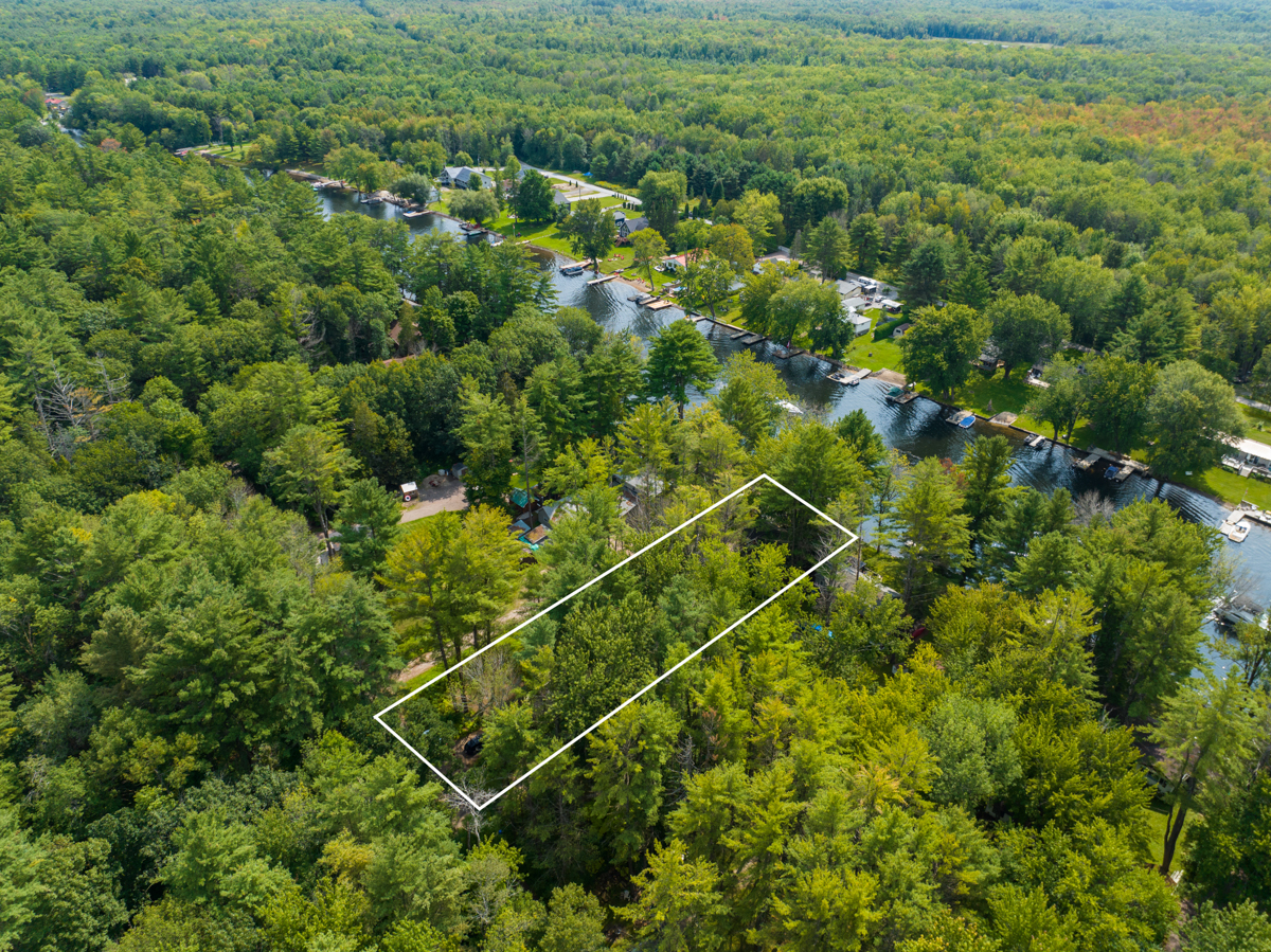 Overhead view of a waterfront river area with lots of green trees and cottages. A white rectangle shows the property area of the cottage.