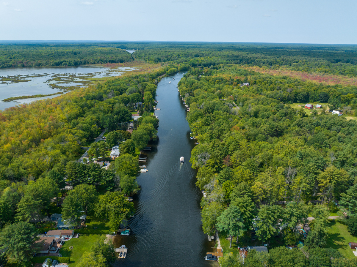 Overhead view of a river lined with cottages and green trees on either side.