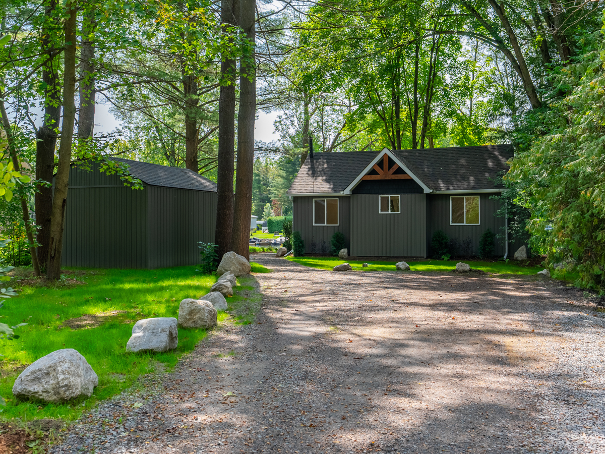 A dirt driveway in front of a small cottage property with a detached garage.
