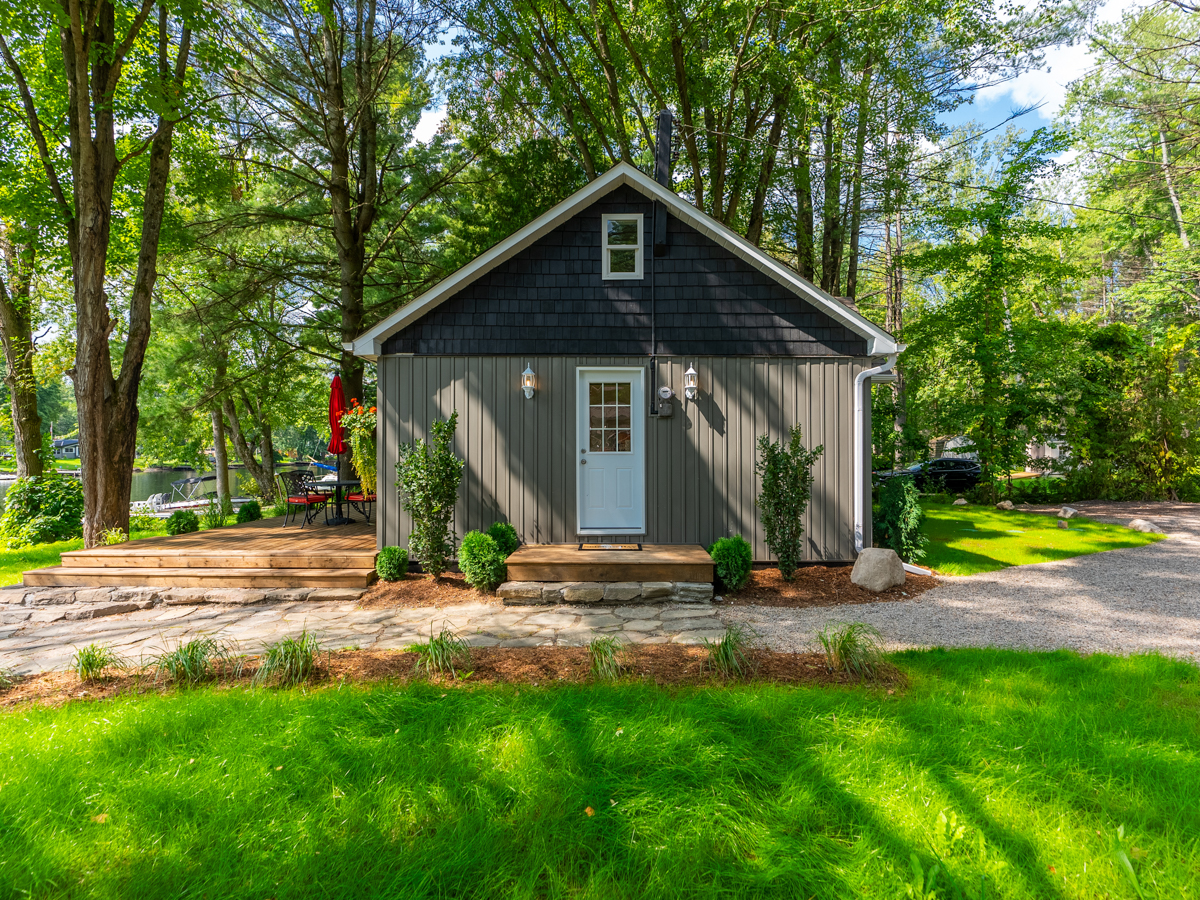 The side of a small cottage, with a patio walkway and a white door to the inside.