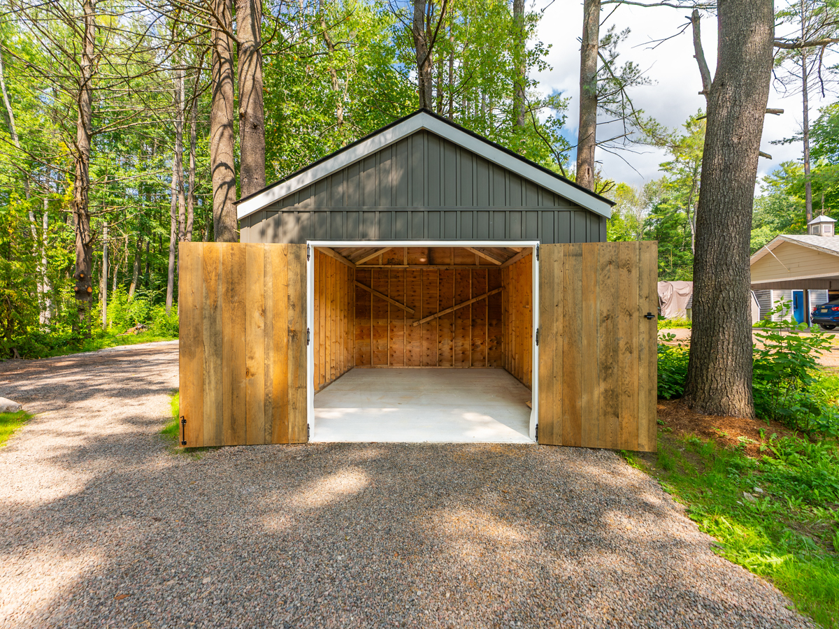 A new detached garage with wooden double doors, which are open to show an empty interior.