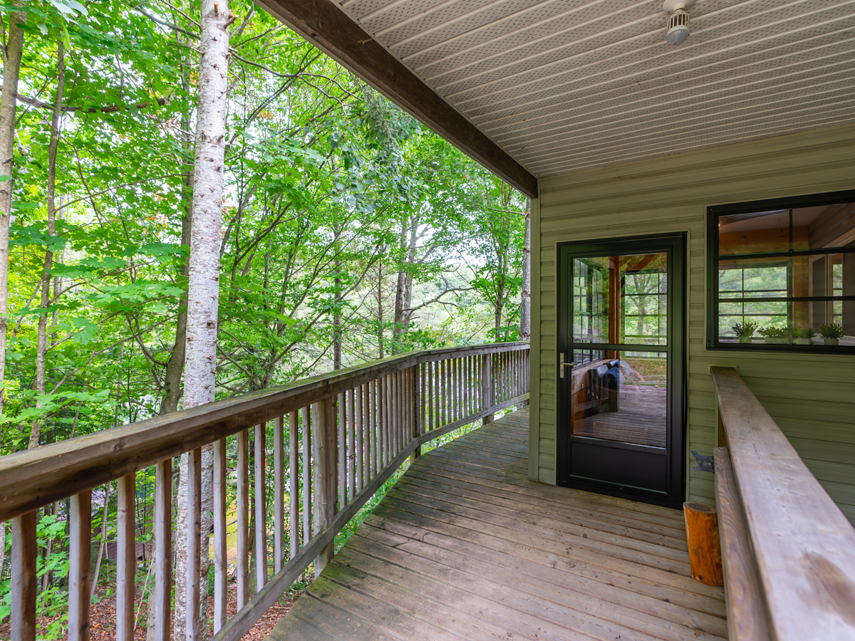 A covered porch leads to the front entrance of a cottage and wraps around to a deck.