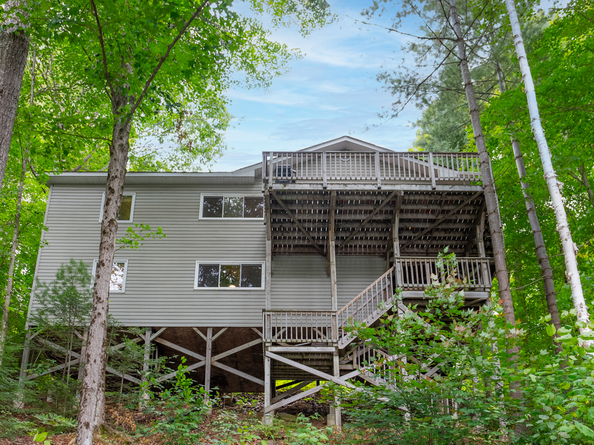 A cottage with two levels, each with a deck, surrounded by trees.