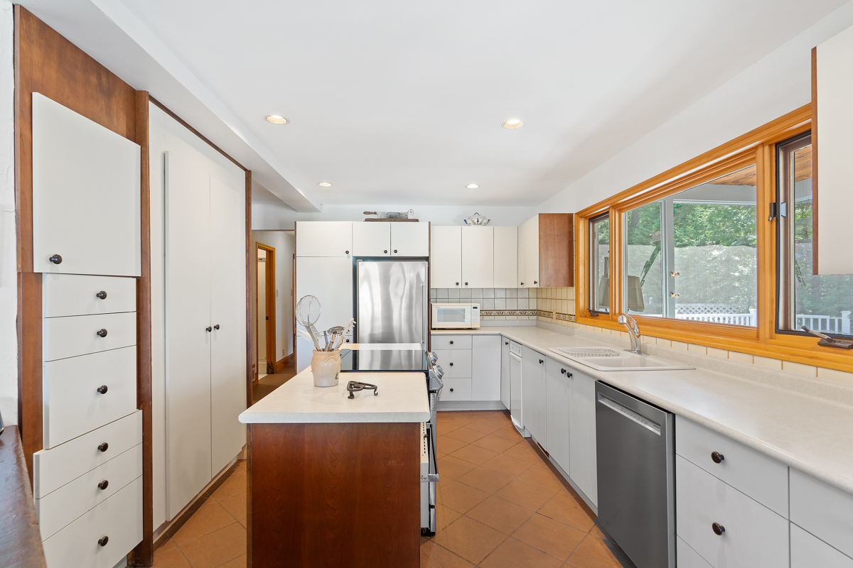 A bright kitchen with an island, white cupboards, and stainless steel appliances.