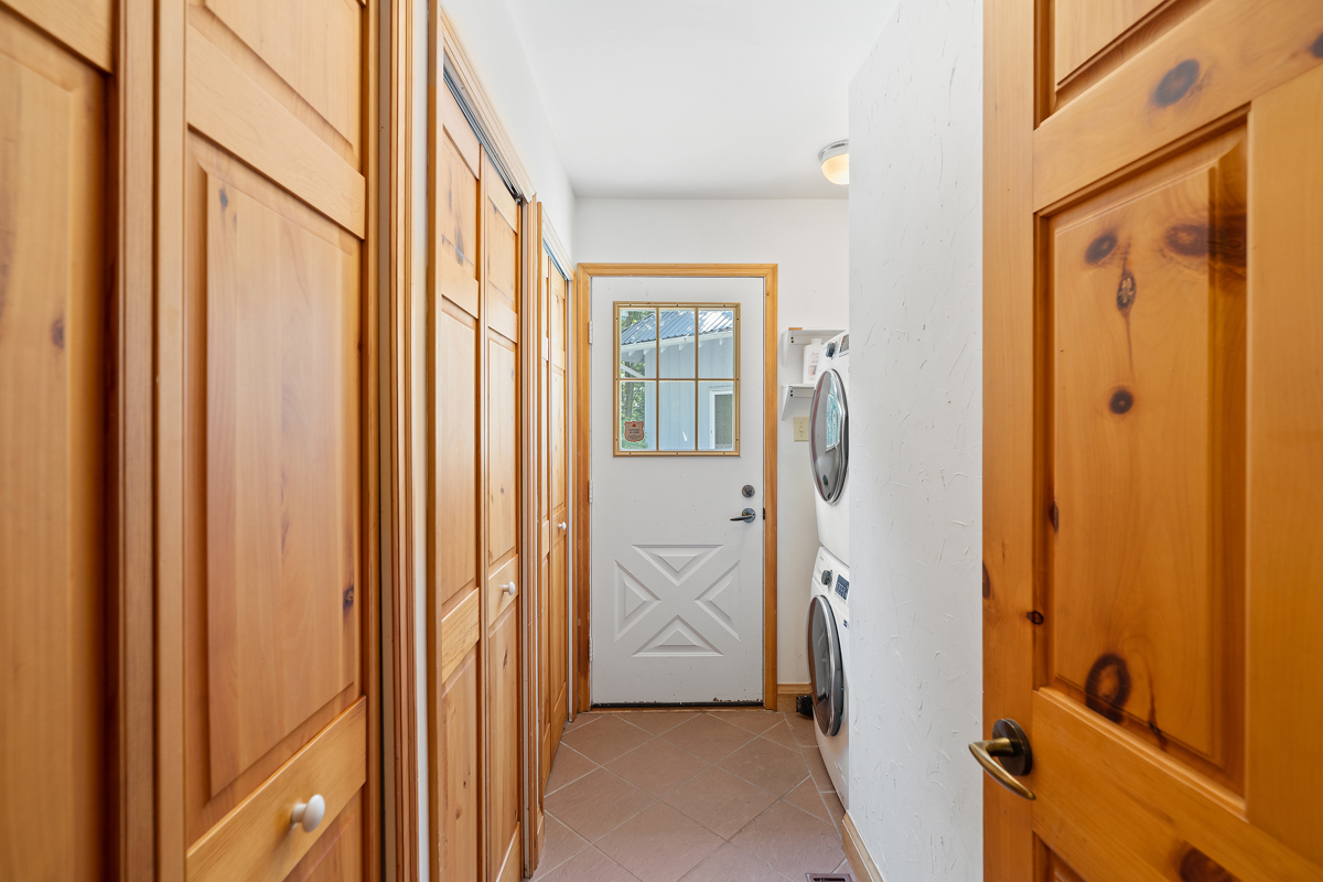 A narrow hallway leads to a small area with a stacked washing machine and dryer, and a door to outside.