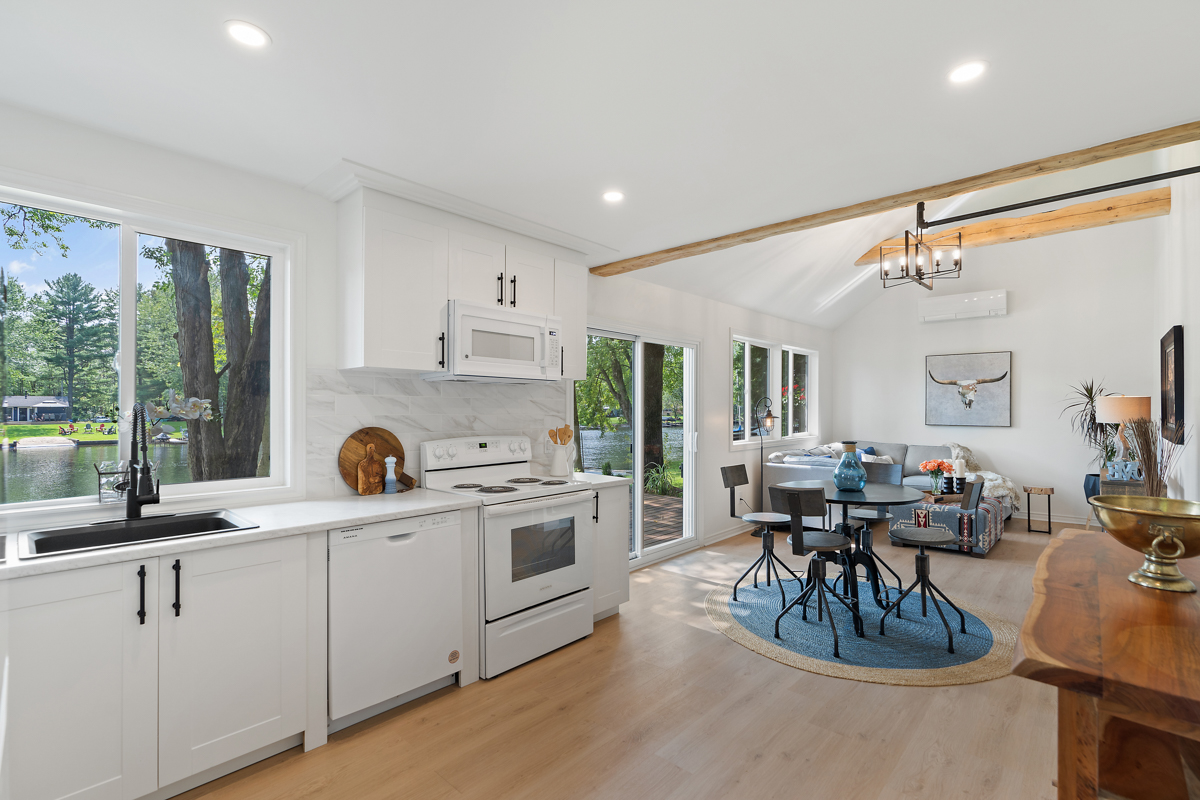 A bright, open-concept kitchen and dining area with hardwood floors, in a cottage.
