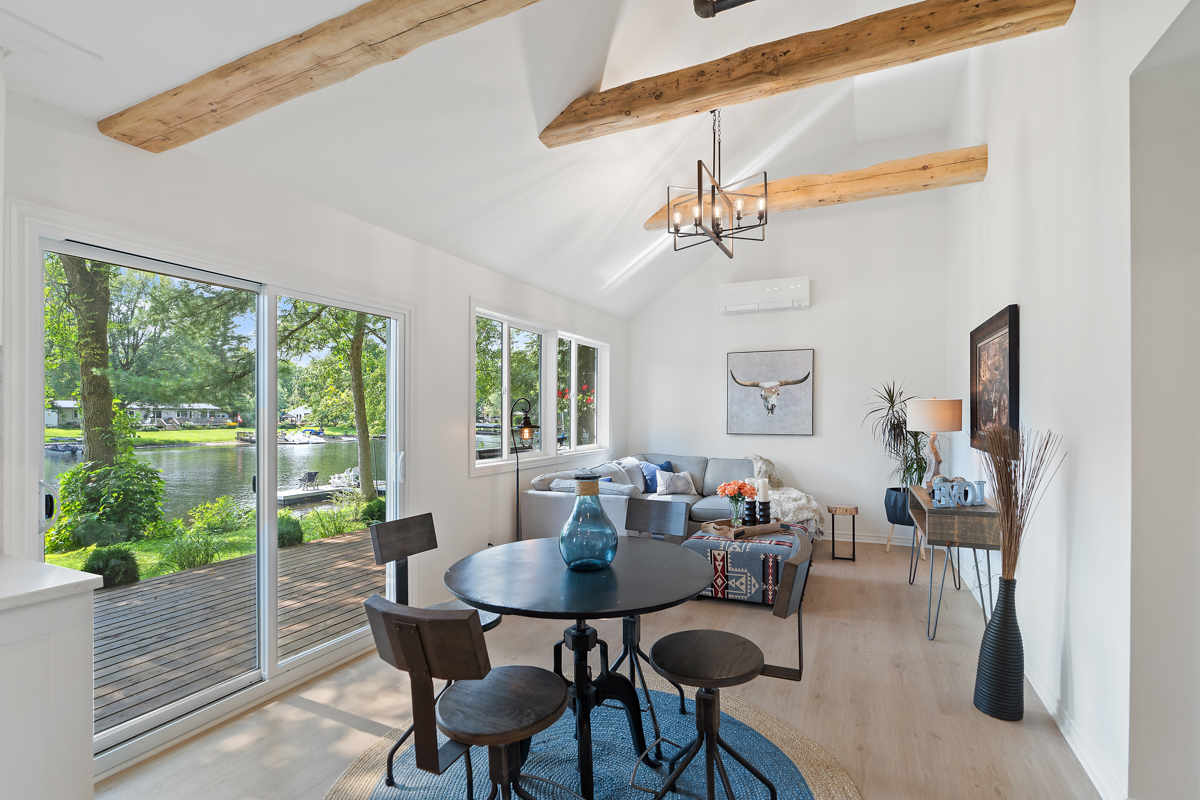 A bright, open-concept dining and living space in a cottage. Double glass doors open up to a deck.