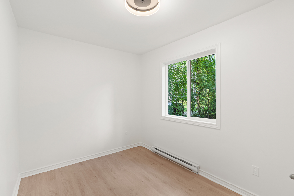 An empty bedroom with hardwood floors and white walls.