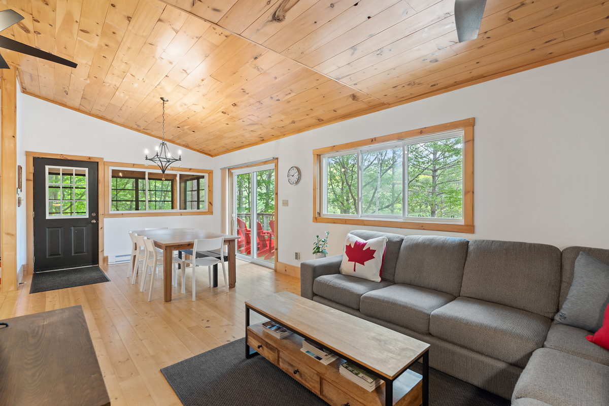 A main floor area with wood-panelled ceilings, an L-shaped couch, a coffee table, and a dining area with a table and chairs..