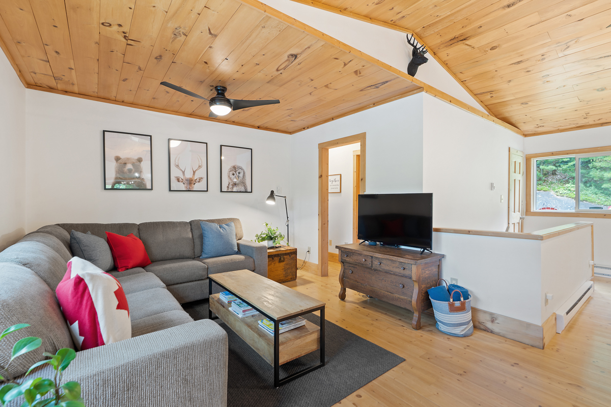 A living area with wood-panelled ceilings, an L-shaped couch, and a television.