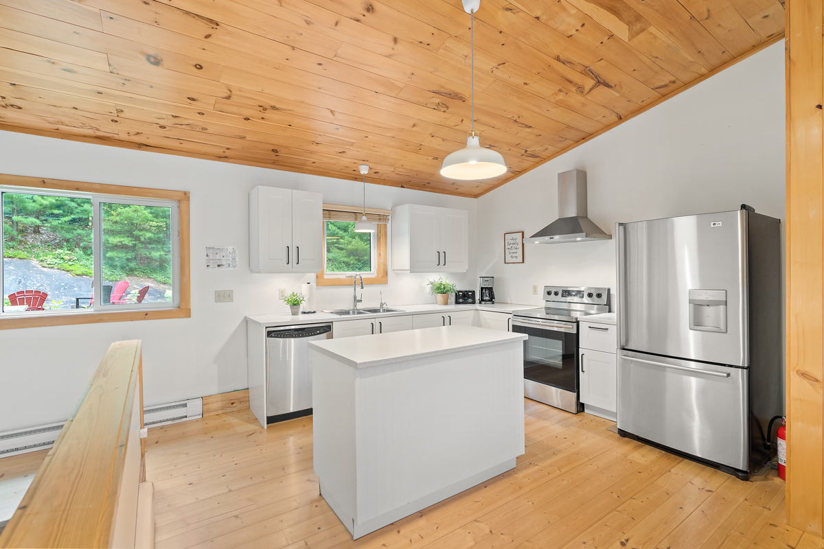 A bright cottage kitchen with wood-panelled ceilings, white cabinets, and modern appliances.