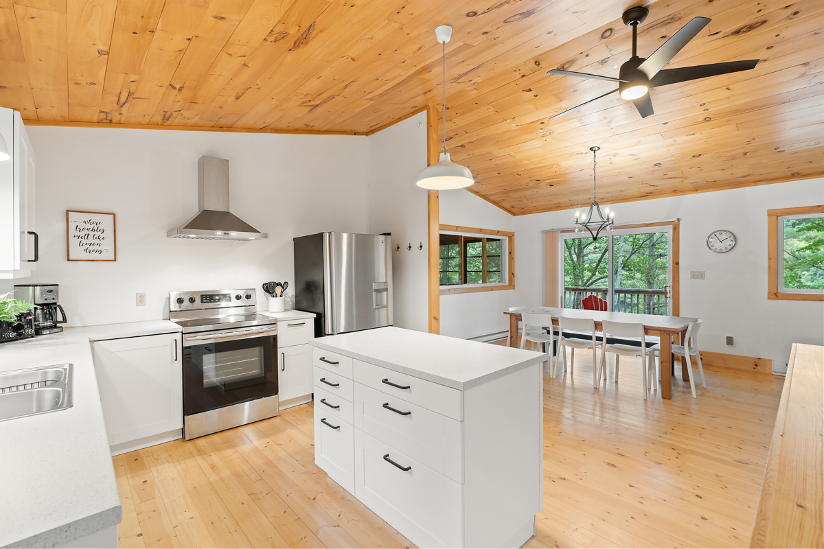 A bright cottage kitchen with wood-panelled ceilings, white cabinets, and modern appliances.
