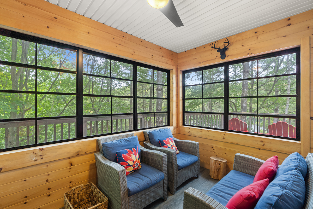 A sunroom with large windows, wood-panelled walls, a couch and two chairs.