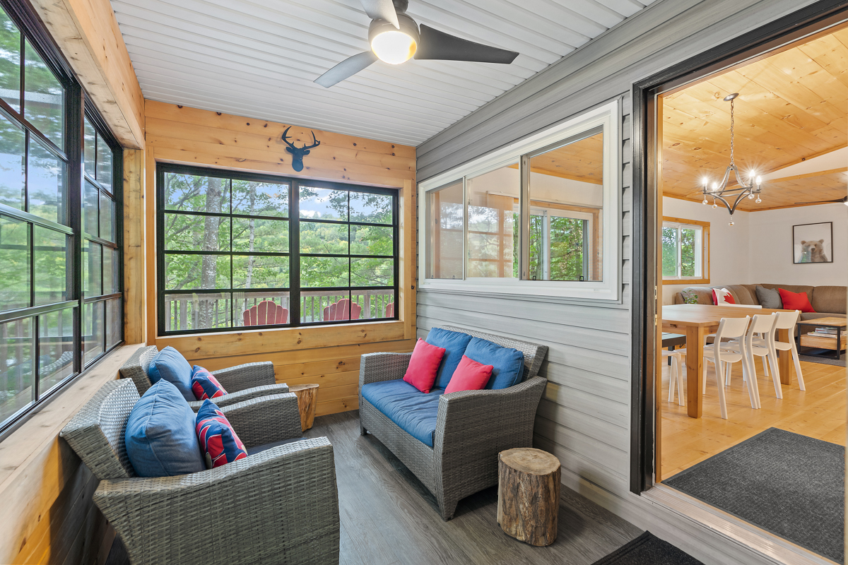A sunroom with large windows, wood-panelled walls, a couch and two chairs.