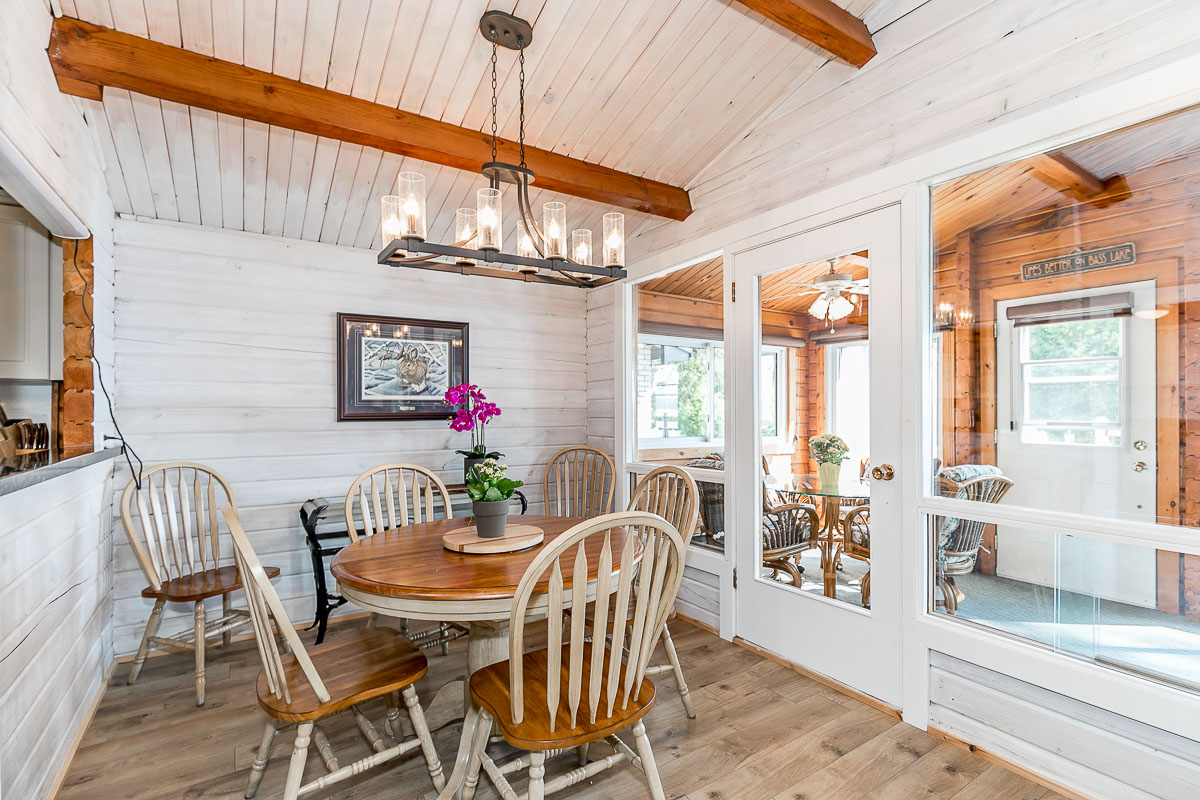 A small, bright dining area with a table and chairs. A door beside the table leads to a long sunroom with lots of windows.