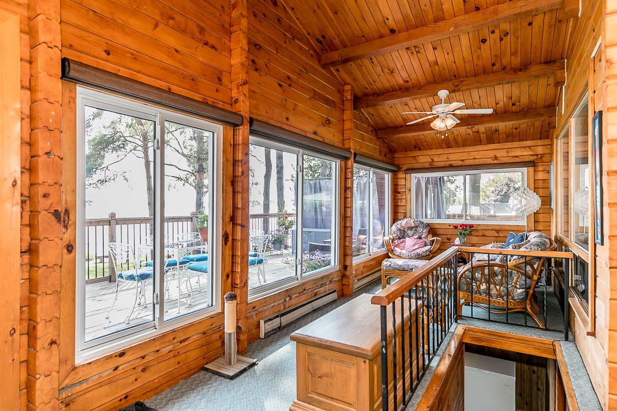 A long sunroom with lots of windows, seating, and stairs leading down to a basement.