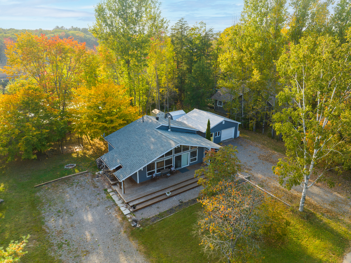 Overhead view of a bungalow cottage with a large driveway, surrounded by trees.