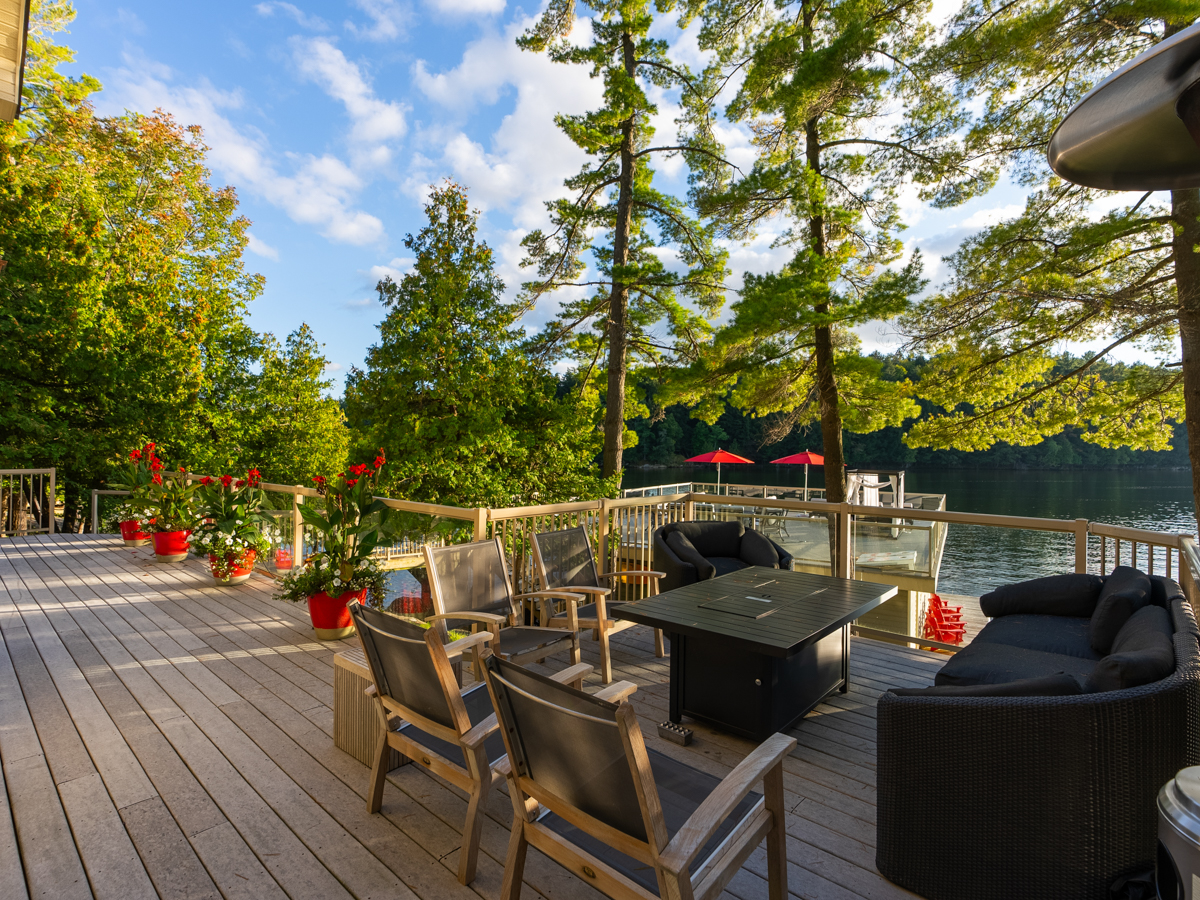 Chairs sit around a fire table on a deck looking out to a lake.