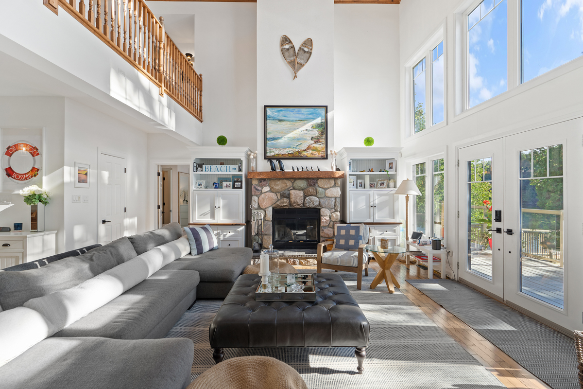 A bright, open lake house living space with vaulted ceilings, lots of windows, a stone fireplace, and plenty of seating.