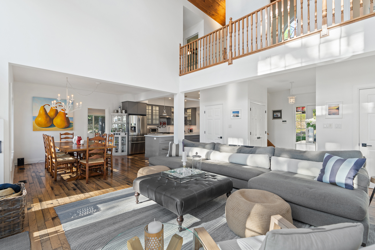 A bright, open lake house living space with vaulted ceilings, lots of windows, and plenty of seating, leading into a kitchen and dining area.