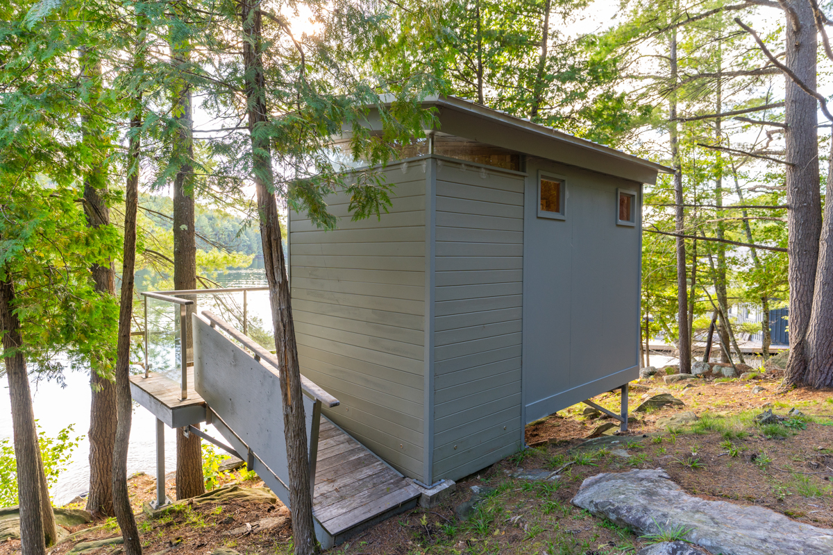 A small building on the waterfront edge of a tree-lined property,