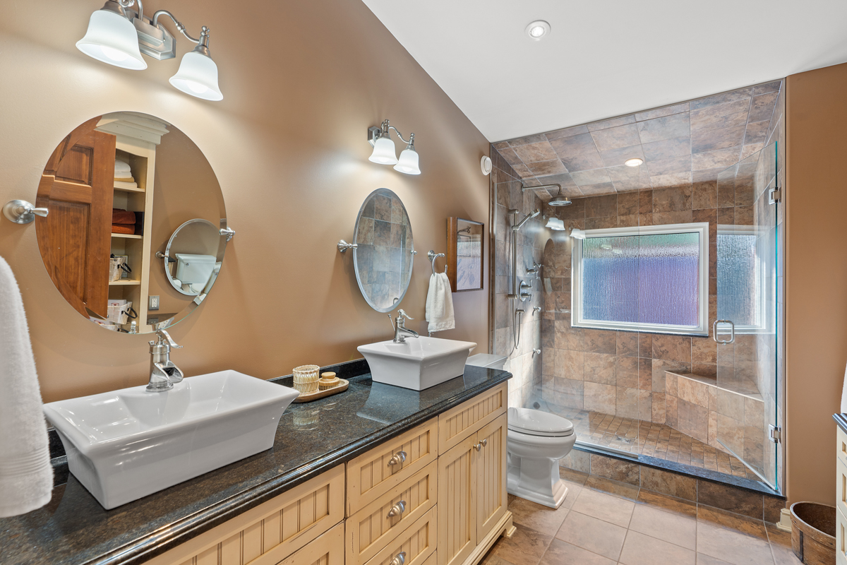 A big bathroom with double sinks, a toilet, and a walk-in shower.